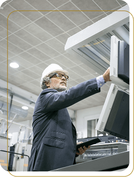 A professional technician in a white safety helmet and suit operating advanced industrial control panels in a manufacturing facility.