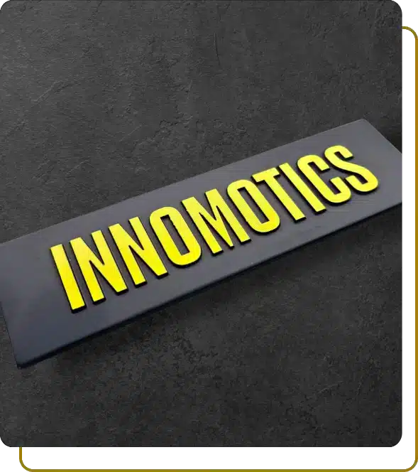 Yellow anodized 3D aluminum INNOMOTICS logo with raised letters on a black background.
