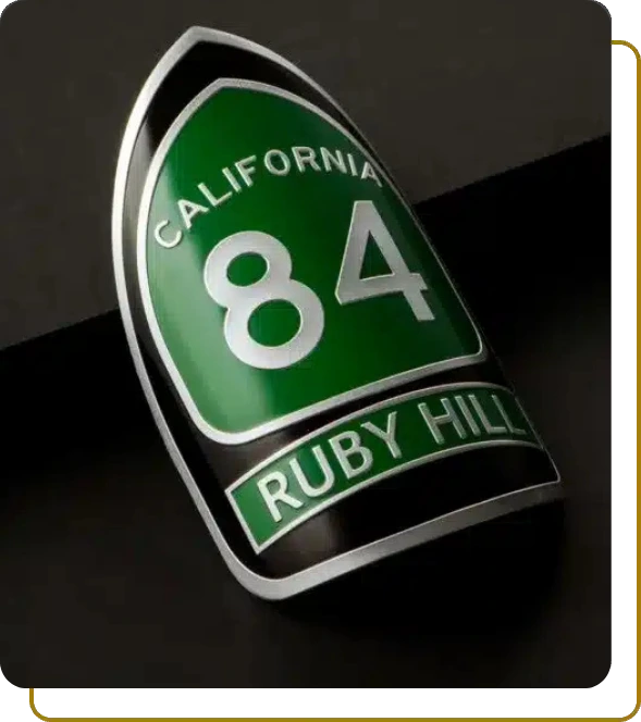 Shield-shaped 3D aluminum label with 'California 84 Ruby Hill' text on a curved black surface.