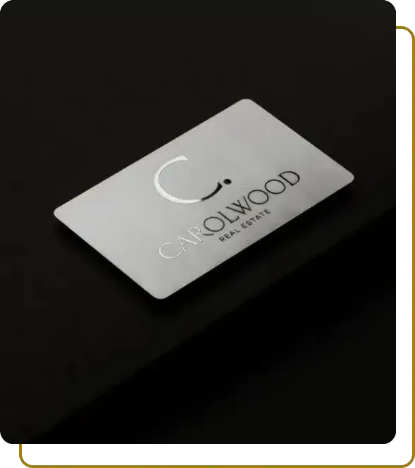 Brushed stainless steel business card for CAROLWOOD Real Estate with precision etched branding on a dark surface.
