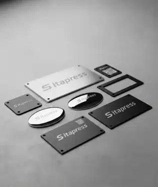 A collection of various SITAPRESS metal products including rectangular nameplates, oval tags, and laser-marked parts in different finishes.