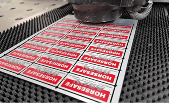 Perforovaný červený kovový plech s opakovaným označením „HORSESAFE" po mechanickom dierovaní